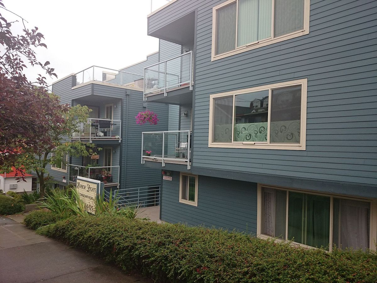 The walkway between the two Harbor Lights West buildings, with stepped balconies, hanging flower baskets, and clipped hedges along the sidewalk.